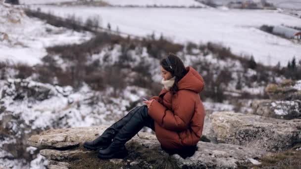 Молодая Привлекательная Красивая Девушка Зимней Одежде Сидит Вершине Скалы Невероятным — стоковое видео