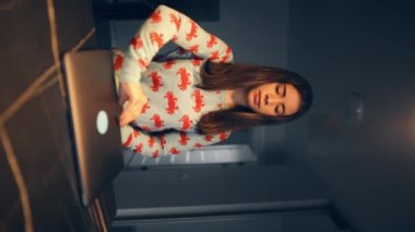 Genç bir kadın dizüstü bilgisayarı açar ve mutfakta otururken çalışmaya başlar. Dikey video