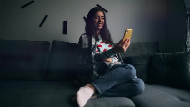 一位年轻女子坐在客厅的沙发上 兴高采烈地通过智能手机视频通话 — 图库视频影像