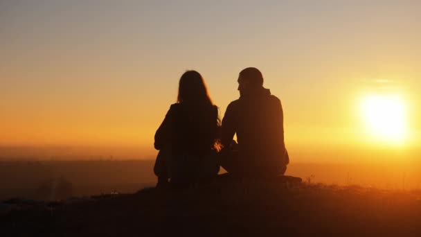 一对夫妇在山顶夕阳西下的轮廓 一个男人和一个女人坐在一起 欣赏日落和令人难以置信的风景 在一起共度时光 这是一次约会 — 图库视频影像