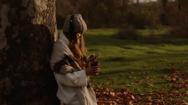 Young Cute Woman Headphones Leaning Tree Autumn Park Uses Smartphone — 图库视频影像