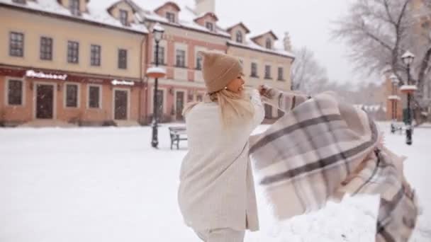 カメラは 雪の中街を走る若い魅力的な笑顔の女の子を追いかけ カメラを見て回り 都市の建物や空を背景に楽しみ クリスマス気分 — ストック動画
