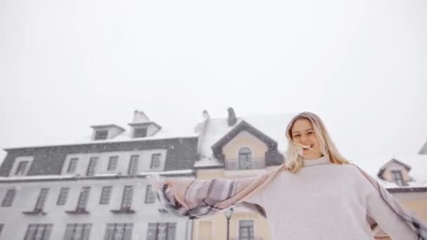 在雪地的房屋和天空的衬托下 年轻貌美迷人的姑娘欢快地在雪地里打转 在照相机前 在圣诞假期里 在新年快乐地微笑着 — 图库视频影像