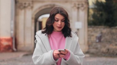 Close-up portrait of a young attractive cute woman girl typing on a smartphone and then looking at the camera and smiling sweetly