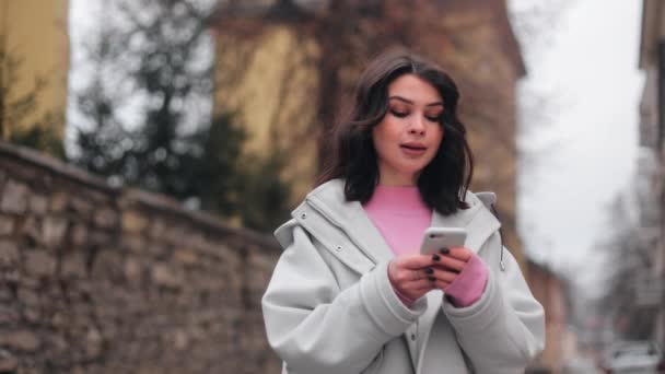Jovem Menina Atraente Usando Smartphone Enquanto Está Rua Cidade Pulando — Vídeo de Stock