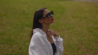 Young attractive beautiful gorgeous European Ukrainian female fashion model long haired brunette slowly moving her face looking at camera staying outdoors in park. High quality 4k footage