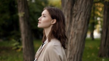 Close-up portrait of beautiful elegant confident smiling young brunette woman in business clothes standing in autumn park.