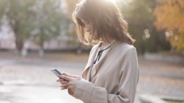  beautiful lady, elegant confident young brunette woman in business clothes working using mobile phone smartphone standing on autumn city street. High quality 4k footage