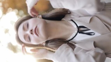 Vertical video view. Close up face portrait of young beautiful elegant pleasant woman girl model looking at camera and fixing her brunette hair playing with hair in sunlight. 