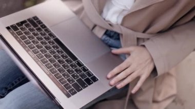 Smiling female manager finishing her works closing laptop computer looks aside dreamly while sitting on the curb on an autumn city street in sunlight. High quality 4k footage