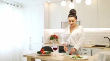Young beautiful woman in jeans preparing healthy dinner at home in the kitchen, tasting salad