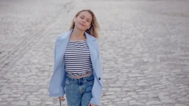 Close-up portrait of stylish blonde young woman lady girl having fun walking dancing listening to music on city street in sunlight