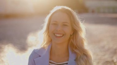 Closeup face of beautiful blond sexy smiling woman with long hair. Portrait of gorgeous girl looking to camera. A happy girl in the rays of the sun close-up laughs very hard
