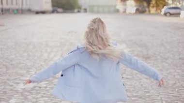 the camera follows a pretty blonde girl with long hair who runs happily and turns to the camera smiling. cheerful young stylish woman