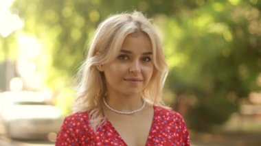 Close up face of beautiful cute pretty blonde, smiling young woman girl in red summer dress.  Portrait of a gorgeous girl looking at the camera on a city street