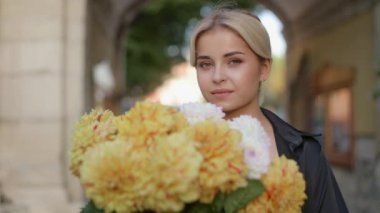 Close up portrait of a young pretty smiling cute girl with a huge bouquet of flowers standing outside on a sunny autumn day