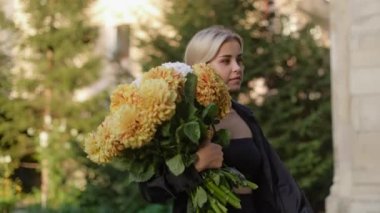 A young, stylish, beautiful elegant woman carries a huge bouquet of flowers and walks down the street of the old town