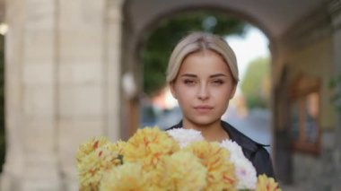 Close up portrait of a young pretty smiling cute woman with a huge bouquet of flowers walking down the street on a sunny autumn day