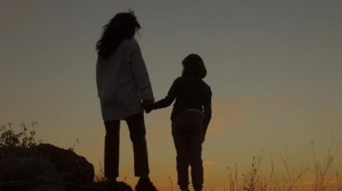Silhouette of a mother and daughter holding hands and hugging on the background of the sky at sunset.  Rear view.  Family, love, hugs