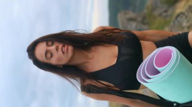 young woman girl with an athletic body carrying a bag and a mat in sportswear walking on a mountain with a beautiful view for outdoor yoga or fitness, morning exercises. Vertical video