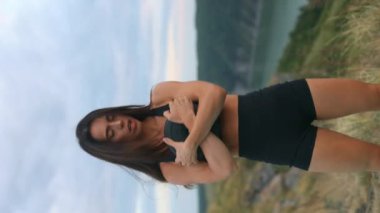 Spor kıyafetleri içinde genç ve güzel bir kadın dışarıda kettlebell ile vücut büküyor, sabah sporu yapıyor. Dikey video