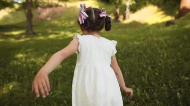 Kız parkta koşuyor. Çocuk oynuyor, uçuyormuş gibi koşuyor. Kamera çocuğu yavaşça takip ediyor, koşuyor ve etrafa bakıyor. Kırsal kaygısız çocukluk. Tatlı güzel kız.