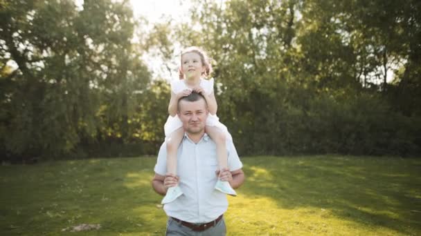幸福的家庭父亲把孩子抱在肩上 快乐的小女孩坐在父亲的背上玩耍 父母对孩子的照料 父亲节 家庭户外散步 — 图库视频影像