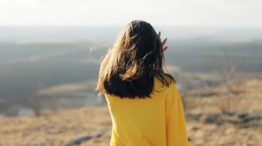 Uzun saçlı tatlı esmer bir kadın bir tarlada kameraya bakıyor. Mutlu bir kız mutlu bir gülümsemeyle kameraya bakıp flört ediyor. Dağın tepesinde yürüyorum. duygular 