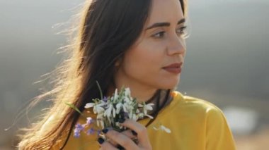 Kar damlalarını koklayan güzel bir kadının portresi. Güneş ışığında elinde bir buket çiçekle gülümseyen bayanın yakın çekimi. Mutlu bir kızın yüzü, rüzgar saçlarını savuruyor.