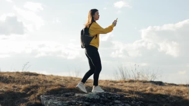 穿着黄色毛衣 背着背包的女游客们试图用脚尖站着的方式捕捉她在山上的手机信号 但没有信号 — 图库视频影像