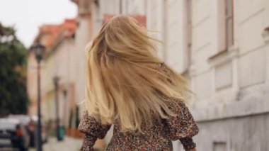 Genç, güzel, gülümseyen bir kızın portresi. Uzun saçlı, şık bir elbiseyle şehirde yürüyor. Güneşli bir sonbahar gününde saçları rüzgarda uçuşuyor.