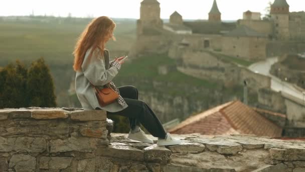 Μια Γυναίκα Τουρίστρια Μακριά Μαλλιά Κάθεται Ένα Πέτρινο Φράχτη Μπροστά — Αρχείο Βίντεο