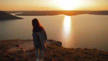 Kız, akşam günbatımında nehrin büyüleyici manzarasını görmek için uçurumun kenarına yürür. Deniz kenarındaki yüksek bir dağda gün doğumuyla karşılaşan kadın karakter. Harikalar diyarı.