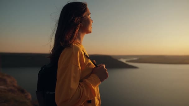 一个年轻的有灵感的女人站在海面上的一座岩石山上 或者在美丽的日落的天空中 举起她的手 观光客欣赏日落 景色令人难以置信 — 图库视频影像