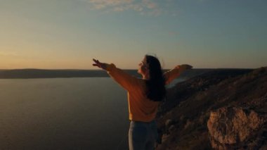 Kamera, bir dağın tepesinde akan bir nehrin üzerindeki uçurumun kenarında duran ve gün batımına kavuşmak için kollarını kaldıran genç ve güzel bir kadının etrafında döner. Mutlu ve hayattan sarhoş