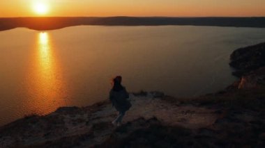 Gün batımında kemerli bir kanyonun üzerindeki uçurumun kenarına koşan ve kollarını yana kaldıran genç bir kadının sinematik görüntüsü, gezgin inanılmaz manzaraya hayran kalıyor.
