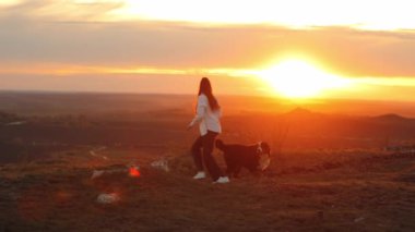 Bernese Dağ Köpeği (Bernese Dağ Köpeği) Beyaz gömlekli uzun saçlı tatlı bir kız inanılmaz bir manzaranın arka planında bir köpekle dışarıda oynuyor. Bir kız evcil hayvanını eğitir