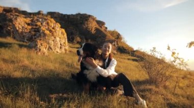 Bernese Dağ Köpeği (Bernese Dağ Köpeği) Büyük köpeği olan genç bir kız dışarıda parkta oynarken eğleniyor. Bir genç, köpeğini yüzyüze kucaklar ve birlikte mutlu vakit geçirir.