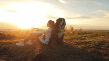 Bernese Dağ Köpeği (Bernese Dağ Köpeği) Çekici genç kız gün batımına hayran bir şekilde yürürken ya da seyahat ederken büyük köpeğine yaslanıyor. Hayvanlarla seyahat etme kavramı.