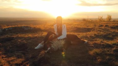 Bernese Dağ Köpeği (Bernese Dağ Köpeği) Çekici genç kız yürürken ya da seyahat ederken büyük köpeğiyle oynuyor, gün batımını izlerken köpeğin karnını okşuyor..