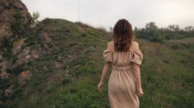 Tarlada çimenlerde koşan kırsal tarzda giyinmiş çekici bir kadın kameraya dönüyor ve gülümsüyor. Bir yaz gününde eğlenmek.