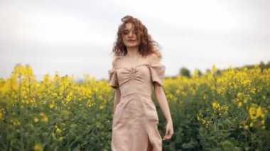 Özgür kız kolza tohumu tarlasında, tarımda, çocukluk hayali konseptinde mutlu bir şekilde koşuyor. Çiftlik kızı, mutlu genç güzel bir kadın tarlada koşuyor, kameraya dönüyor, uzun kahverengi saçlı.