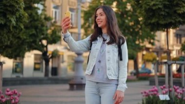 Genç, gülümseyen çekici bir kız, Lviv şehrinde yürürken akıllı telefon kullanan bir arkadaşıyla konuşuyor. yavaş çekimde.