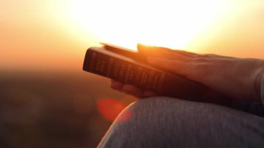 Gün batımında bir kadının elinde İncil 'in yakın çekimi. Hıristiyanlık