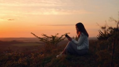 Bir kız açık havada İncil okuyor. Bir kadın elinde bir İncil tutuyor ve gün batımında bir tarlada otururken Tanrı 'nın kelamını okuyor.