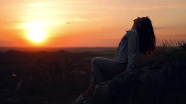 Uzun saçlı mutlu bir kadın gün batımında bir akşam tarlasının tazeliğinden zevk alır. Batan güneşin arka planında gevşek saçlı bir kadın profili silueti. Rüzgâr saçında