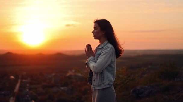 少女は日没時に祈りのシルエットで手を折りました 外で祈ってる女性 女性は神に祈り 罪の赦しと世界の平和を求めています — ストック動画