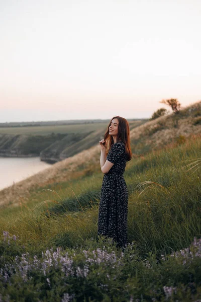 Güzel, genç, esmer bir kız kır çiçeklerinin arasında duruyor ve elinde bir çiçek filizi tutuyor, başka tarafa bakıyor ve gülümsüyor. Yazın sevimli portresi, hoş bir yüz neşeli ve samimi.