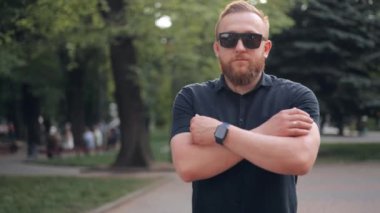 Şehirde yürüyen mutlu sakallı adam. Kollarını göğsünün üzerinde çapraz yapar. O bir gömlek ve güneş gözlüğü takıyor. Kameraya bakar ve gülümser.. 