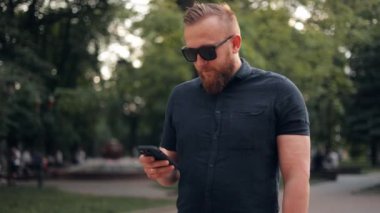 Başarılı bir adam telefonu kullanıyor, internette sohbet ediyor, şehir caddesinde duruyor. İş adamı akıllı telefona bakıyor ve iyi haberlerle gülümsüyor.